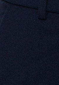 Gros plan d'un tissu bleu marine foncé avec une boucle de ceinture visible et une couture, probablement partie d'un vêtement comme un pantalon ou une jupe.
