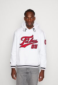 Felpa bianca con cappuccio e ricamo rosso che presenta la scritta "Fubu" e "05". Stringhe regolabili, polsini e orlo a coste, tasca a kangaroo sul davanti.