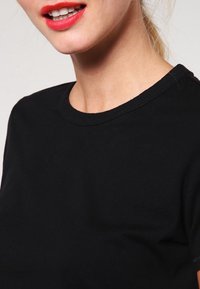 Black cotton t-shirt with a round neckline, short sleeves, and a smooth texture. Features a simple design without patterns or accents.