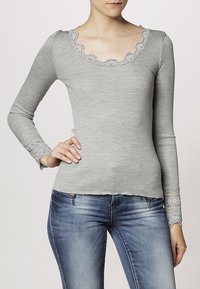 Grå långärmad topp med ribbad textur, scallop-mudd, och spetsdetaljer på ärmarna, kombinerad med blå denimjeans.