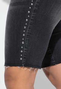 Sorte denim shorts med en rå kant, prydet med sølvfarvede nitter langs siden for ekstra detaljer.