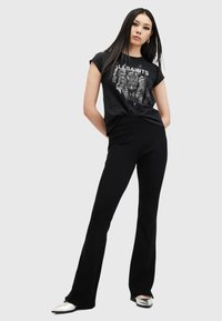Camiseta gráfica negra con estampado de tigre y logo, combinada con pantalones negros acampanados. El modelo lleva zapatos de punta plateados.