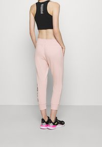 Ljusrosa joggers med elastisk midja och mudd, med sidofickor och svarta tryckta detaljer. Matcher med svarta sportskor.