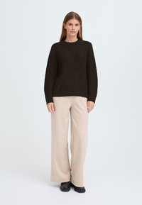 Brown knitted sweater with textured pattern and ribbed hem, paired with light beige wide-leg pants and black shoes. Simple, modern design.