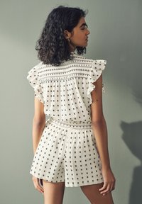 Vit rompers med svarta geometriska mönster, volang ärmar, smockad byst och elastisk midja. Lätt, texturerad tyg.