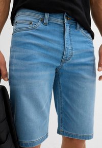 Shorts en denim bleu clair avec une coupe droite et un ourlet brut. Comprend cinq poches et des détails de couture contrastants.