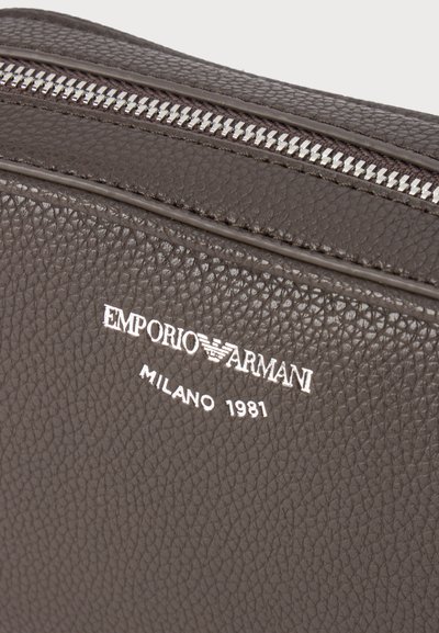Σκούρο καφέ δερμάτινη υφή με ασημένιο φερμουάρ και λευκό λογότυπο Emporio Armani Milano 1981.