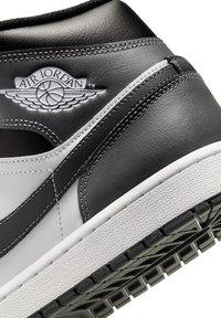 Sapatilha de couro preta e branca com sola texturizada, apresentando um logo Air Jordan grisalho no calcanhar e detalhes em costura contrastantes.