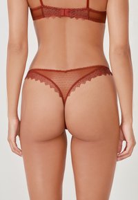 Rote Spitze-Lingerie mit transparentem Mesh-Design, das mit gewellten Kanten und einem Punktenmuster verziert ist. Verstellbare Träger und ein Rückenteil im Tanga-Stil.