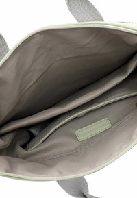 Lichtgroene tote bag met een ritsluiting. De binnenkant heeft een gladde beige voering, één ritszak en een label met de merknaam.