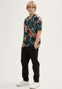 Maglietta nera a maniche corte con un vivace motivo floreale, abbinata a pantaloni neri e sneakers bianche. Vestibilità casual e tessuto leggero.