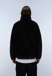 Μαύρο φλις μπουφάν με ψηλό γιακά και υφή. Διαθέτει εντυπωσιακά μαύρα υφασμάτινα στοιχεία στους ώμους και τους καρπούς.