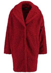 Červený plyšový teddy kabát s texturou, se střiženým límcem a otevřeným předním dílem. Má volné rukávy a měkký chlupatý materiál. Bez viditelných zapínání.