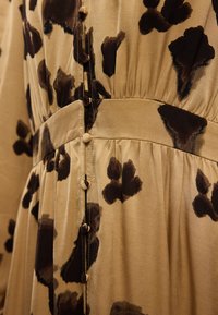 Μπεζ φόρεμα με καφέ σχέδιο ζώου, από λεία ύλη, με συγκεντρωμένη μέση και κουμπιά κατά μήκος του μπροστινού μέρους.