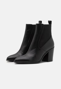 Bottes chevilles en cuir noir avec panneaux latéraux élastiques, bouts pointus et talon épais. Texture lisse avec des détails de couture subtils.