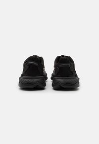 Black athletic shoes with a textured upper, padded collar, and elastic laces. Chunky sole with a wavy tread pattern and prominent branding.