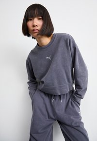 Sudadera gris recortada con un logo sutil, combinada con pantalones de chándal a juego. Textura suave, corte relajado y detalle de cintura con cordón.