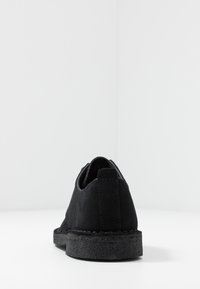 Black suede shoe with a low-profile design, featuring a textured rubber sole, stitched detailing, and a minimalistic heel tab.