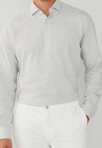 Camicia a maniche lunghe a quadri grigia chiara con abbottonatura e colletto strutturato, abbinata a pantaloni bianchi. Tessuto morbido, design casual.