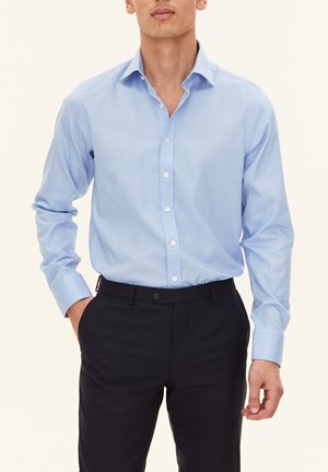 Light blue button-up shirt with a structured collar, long sleeves, and a smooth texture. Paired with dark trousers featuring a front pocket.