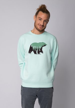 Licht mintgroene sweatshirt met een beren silhouet gevuld met boompatronen. Ronde hals, lange mouwen, zachte stof en een relaxte pasvorm.