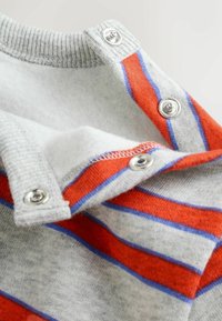 Sivý pletený sveter s červenými a modrými pruhmi, so zapínaním na cvoky pri golieri a mäkkou vnútornou textúrou.