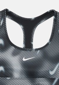 Sutiã desportivo com um padrão riscado preto e branco, feito de material elástico, com um decote redondo e um logo da Nike em branco.