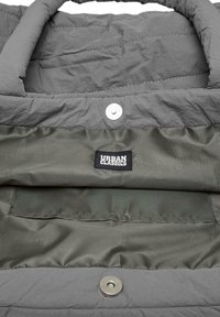 Interno di un giubbotto oversize grigio con tessitura cucita, dotato di fodera verde e un'etichetta nera Urban Classics. Chiusura a scatto e dettagli delle tasche visibili.