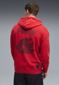 Rode hoodie met een groot zwart "PUMA" logo en een Sonic the Hedgehog grafiek op de achterkant, gemaakt van zacht, gewassen materiaal.