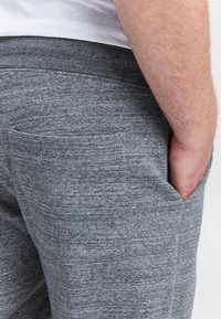 Grijze fleece joggers met elastische tailleband, voorzien van zijzakken en een gestructureerde stof. Close-up zijaanzicht.