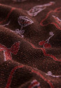 Nahaufnahme von braunem Strickstoff mit roten und weißen Mustern von Cocktailgläsern und Kirschen, die Textur und Falten zeigen.