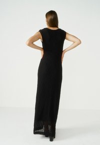 Robe maxi noire avec des plis verticaux, des manches courtes et une silhouette ajustée. Tissu texturé, longueur au sol, avec un ourlet légèrement transparent.