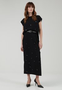 Vestido maxi negro con mangas cortas, que presenta adornos florales y un cinturón brillante. Tejido suave con un corte recto y lados con abertura.