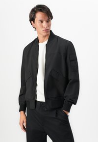 Black bomber jacket featuring a zip closure, ribbed cuffs, and two side pockets. Smooth fabric with minimalistic design details.