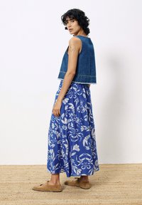Denim cropped vest, blauwe maxi rok met bloemenmotieven en witte patronen, en bruine veterschoenen; achtergrond van een geweven mat.
