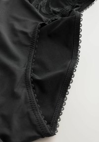 Czarna bielizna z tkaniny z delikatną koronkową lamówką i gładkim przeszyciem na jasnym tle, ukazująca fakturę i szczegółowe krawędzie.