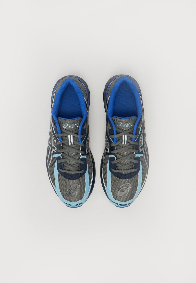 Baskets de sport grises et bleues en mesh, avec une languette rembourrée, des lacets et un logo. Elles possèdent un bout arrondi et une semelle texturée.