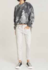 Grå tie-dye sweatshirt med rund halsringning, kombinerad med vita cropped jeans och svarta sneakers med vita sulor och snören.