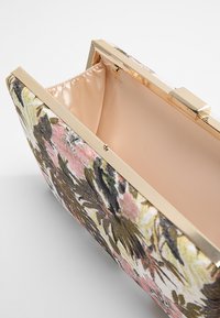 Bolso de mano con estampado floral, exterior de tela suave, cierre en tono dorado y forro beige liso. El espacio interior es libre de obstrucciones.
