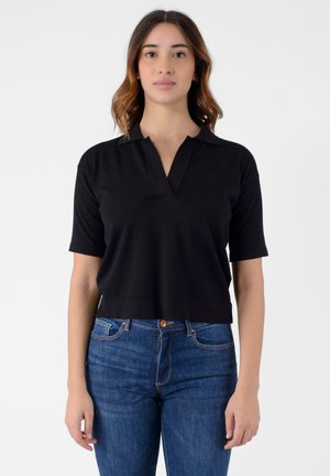 Polo shirt nero a maniche corte con colletto a notched, realizzato in tessuto morbido. Indossato con jeans a vita alta blu scuro, dotati di chiusura con bottone.
