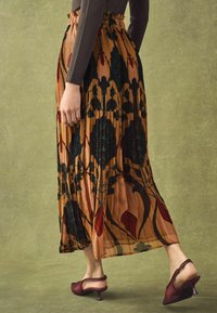 Pleated midi skirt in brown with botanical print in dark green and red. Paired with burgundy heeled shoes with a curved heel.
