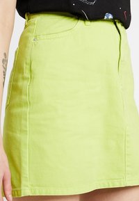 Groene denim mini-jurk met een gladde textuur, voorzien van zijzakken en een getailleerd ontwerp. De stof heeft een subtiele glans bij licht.