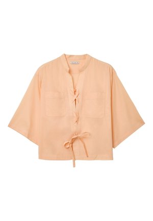 Pfirsichfarbene Bluse mit kurzen Ärmeln, weiten Ärmeln, aufgesetzten Taschen vorne und drei gebundenen Schleifen entlang der Vorderseite.
