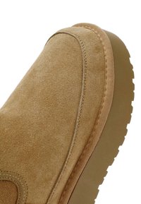 Béžová semišová kotníková bota s kulatou špičkou, texturovaným povrchem, šitými detaily a silnou gumovou podrážkou. Čistý, minimalistický design.