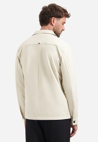 Crème-kleurige jas met een gestructureerde kraag, een gladde textuur en een knoopdetail achterop. Bevat zijzakken en heeft een getailleerde pasvorm.