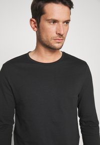 Cămașă neagră cu mâneci lungi și decolteu rotund, confecționată dintr-un material moale din bumbac, cu un design ajustat și fără modele sau accente vizibile.
