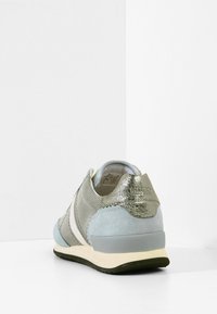 Baskets grises et bleues avec talon métallique, bande blanche sur le côté et semelle noire, présentées en angle de dos sur fond blanc.