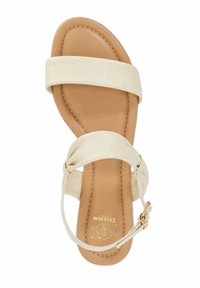 Beige leren sandaal met twee brede banden, amandeltip en een enkelbandje aan de achterkant met goudkleurige hardware. Glad uiterlijk.