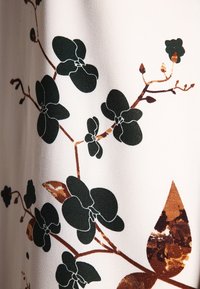 Blommigt tryckt tyg med mörkgröna orkidéblommor på en ljus bakgrund, med bruna accenter och slät textur.