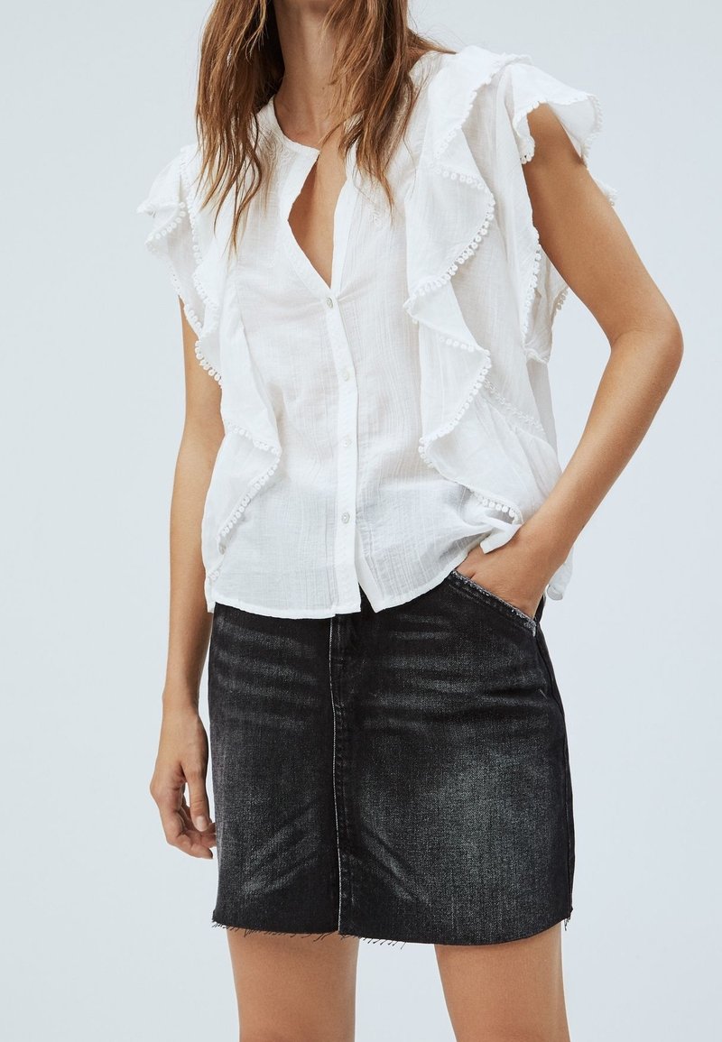 Blouse blanche et légère avec manches à volants et boutonnage devant ; associée à une mini-jupe en jean foncé avec ourlet effiloché.